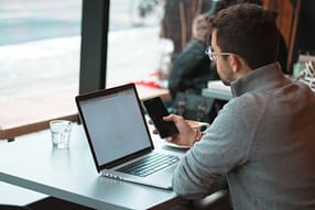 Como testar a velocidade da Internet... 11 man sitting near table with laptop and smartphone near window